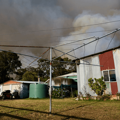Backyard showing a rotary clothes line, water tank and buildings with smoke from a bushfire in the distance